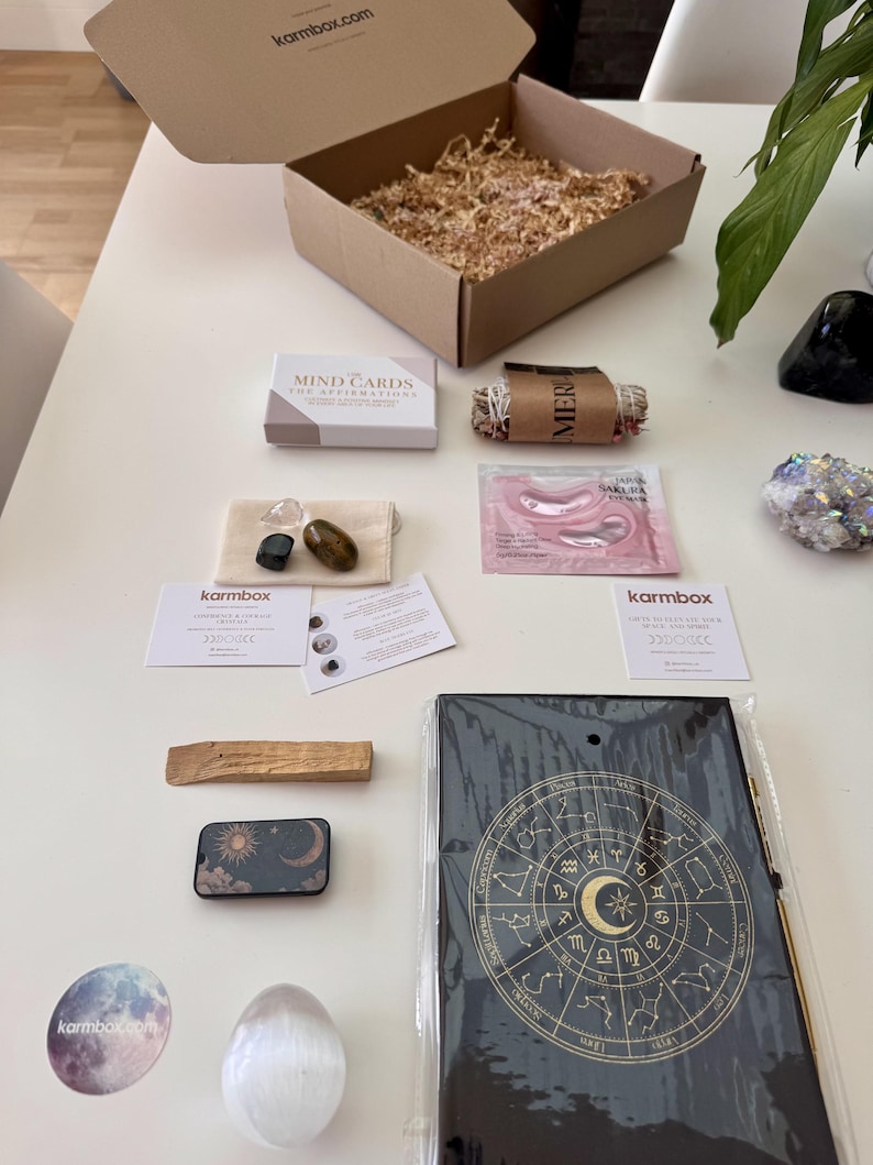 May include: A Karmbox subscription box containing a deck of Mind Cards, a sage bundle, pink Sakura eye masks, three tumbled crystals in a pouch, two informational cards, a palo santo stick, a celestial tin, a moon sticker, a crystal egg, and a zodiac journal.