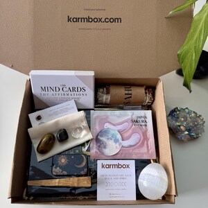 May include: A cardboard subscription box containing LSW Mind Cards, a Japan Sakura eye mask, a bundle of dried herbs, a small pouch with three polished stones, a moon-themed tin, a wooden stick, a white crystal egg, and a Karmbox card.