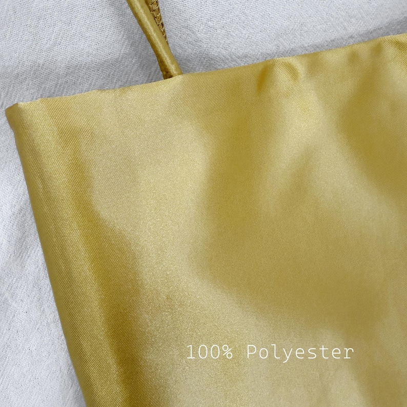 May include: A smooth, solid gold-colored fabric garment featuring a thin strap at the top. The material has a subtle sheen and a visible diagonal weave texture. The text 100% Polyester is printed in white on the lower right side of the fabric.