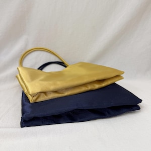 May include: A set of two rectangular satin pouches, one in a vibrant gold and the other in a deep navy blue. Each pouch features a matching circular handle attached to the top edge, with a smooth, reflective fabric finish and clean, folded seams.
