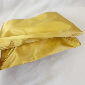 May include: A rectangular pouch crafted from a smooth, lustrous golden-yellow satin fabric. The item features a soft, pliable structure with visible folds and a subtle sheen across its surface, showcasing a consistent monochromatic yellow tone.