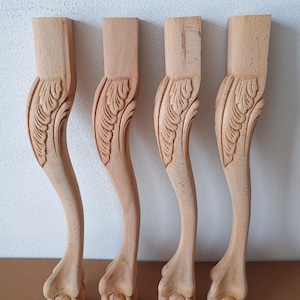 Peut inclure: Quatre pieds de meubles en bois non finis. Chaque pied présente un motif sculpté, une forme incurvée et un pied en forme de patte. Les pieds sont en bois clair, prêts à être teints ou peints. Idéal pour les projets de meubles DIY.
