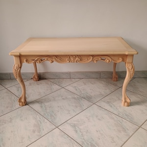Könnte beinhalten: Ein heller Holz-Couchtisch mit aufwendigen Schnitzereien an der Tischplatte und den Beinen. Der Tisch hat eine rechteckige Tischplatte und vier Beine mit einem Krallenfuß-Design.