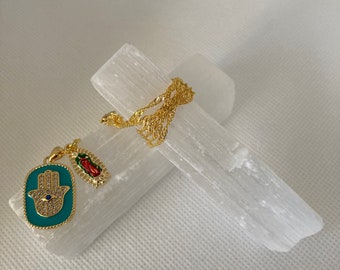 Puede incluir: Collar de cadena dorada con un dije de mano de hamsa turquesa y un dije rojo y dorado. El collar se muestra en un cristal de selenita blanco.