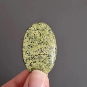 Peut inclure: Pierre précieuse ovale polie, de couleur vert clair, ornée d'un réseau de veines sombres. La pierre présente une surface lisse et brillante. Le motif et la couleur uniques de la pierre précieuse en font une pièce remarquable.