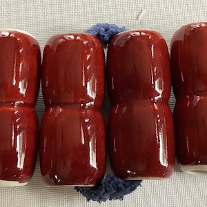 May include: Six dark red ceramic bottle stoppers with white rims. The stoppers are cylindrical and have a slight indentation in the middle.