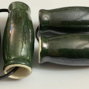 May include: A set of two pairs of dark green ceramic salt and pepper shakers. The shakers have a glossy finish and a classic, rounded shape. The shakers are connected by a black band.
