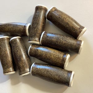 May include: Eight brown ceramic knobs with white trim. The knobs are speckled with brown and have a rounded, cylindrical shape.