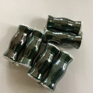 May include: Six dark green ceramic beads with a white rim. The beads have a glossy finish and are slightly irregular in shape.