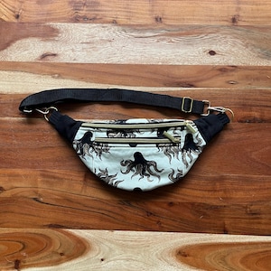 May include: A black fanny pack with an adjustable strap and a zipper closure. The fanny pack is made of a white fabric with a black octopus print.