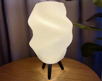 May include: A white, twisted, ceramic lamp with a black tripod base. The lamp is lit and casting a warm glow.
