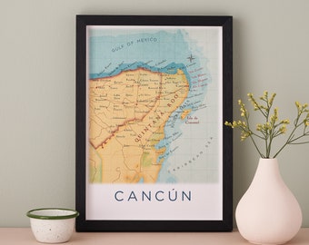 May include: Framed map print of Cancún, Mexico, in a black frame. The map features a vintage style with a color palette of beige, blue, and brown. The word "CANCÚN" is printed in navy blue at the bottom of the print.