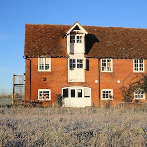 May include: A red brick building with white trim and windows. The building has a gabled roof and a dormer window. The building is surrounded by a field of grass.