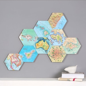 May include: A collection of hexagonal wall art pieces featuring vintage-style world maps. The maps display various regions, including Australia, Hong Kong, and London, with a color palette of blues, greens, and browns. The pieces are arranged in a honeycomb pattern.
