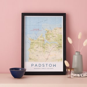 Pode incluir: Um mapa emoldurado de Padstow e o estuário do Camel na Cornualha, Inglaterra. O mapa está em uma moldura preta e tem uma borda branca. O título do mapa é "Padstow" e o subtítulo é "Bancroft Family Holidays".