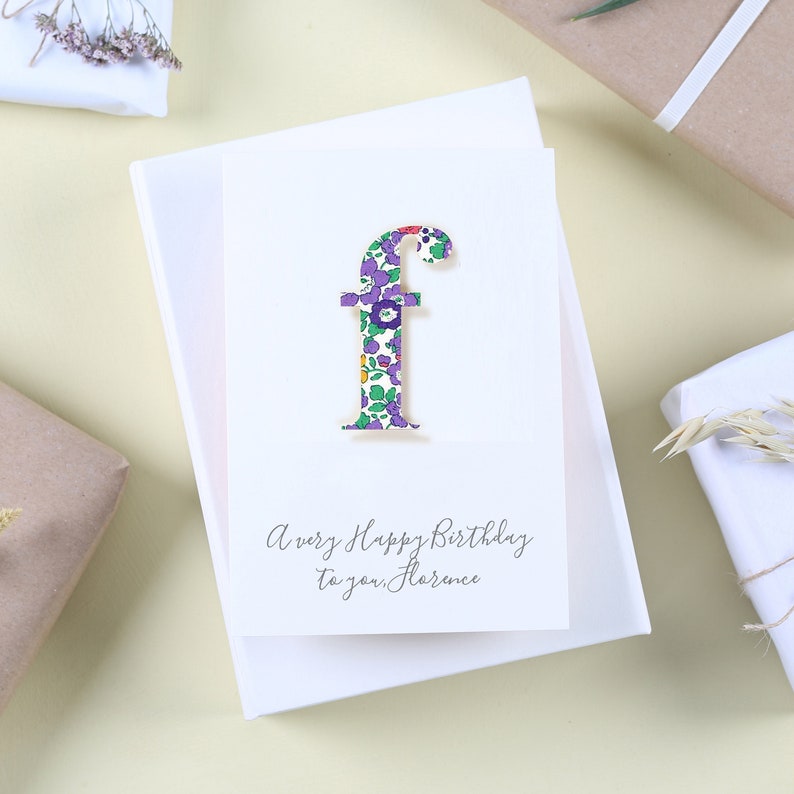 May include: A white card with a floral patterned letter "F" and the text "A very Happy Birthday to you, Florence".
