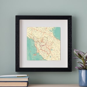 May include: A framed vintage map of the Italian region of Calabria. The map is printed on cream paper with red and brown lines showing roads and rivers. The coastline is shown in blue. The map is framed in a black frame.