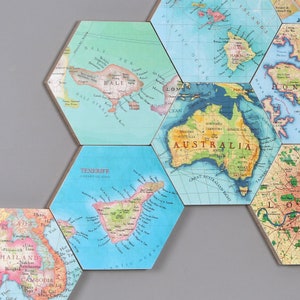 May include: Hexagonal tiles with vintage world map designs. The tiles feature detailed illustrations of various locations, including Bali, Australia, and Tenerife. The maps are in shades of blue, green, and brown, with text labels.