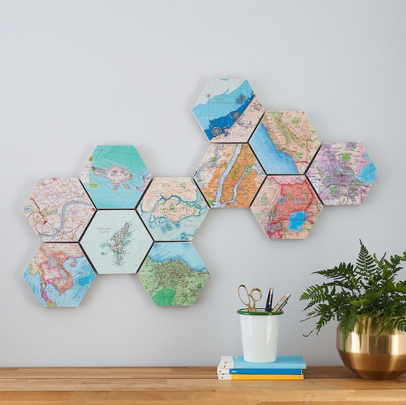 May include: Hexagon-shaped wall art featuring vintage map prints. The arrangement includes maps of various locations, with a focus on cities and regions. The maps are in shades of blue, green, and brown, creating a decorative and educational display. The artwork is mounted on a white wall.