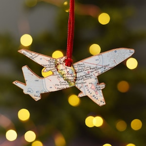 Pode incluir: Um ornamento de avião de madeira decorado com um mapa vintage da Flórida e das Bahamas. O ornamento está pendurado em um cordão vermelho.