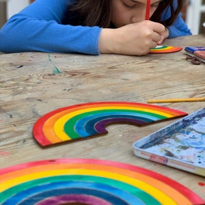 May include: Two wooden rainbow arches painted in vibrant colors of red, orange, yellow, green, blue, indigo, and violet. The arches are on a wooden table.
