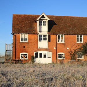 May include: A red brick building with white trim and windows. The building has a brown tiled roof and a white door. The building is surrounded by a grassy area.