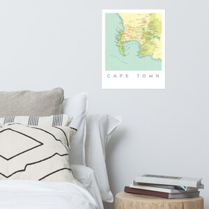 May include: A framed print of a map of Cape Town, South Africa, in shades of yellow, green, and blue. The map shows the coastline, roads, and geographical features. The words "CAPE TOWN" are printed in a clean, sans-serif font below the map.