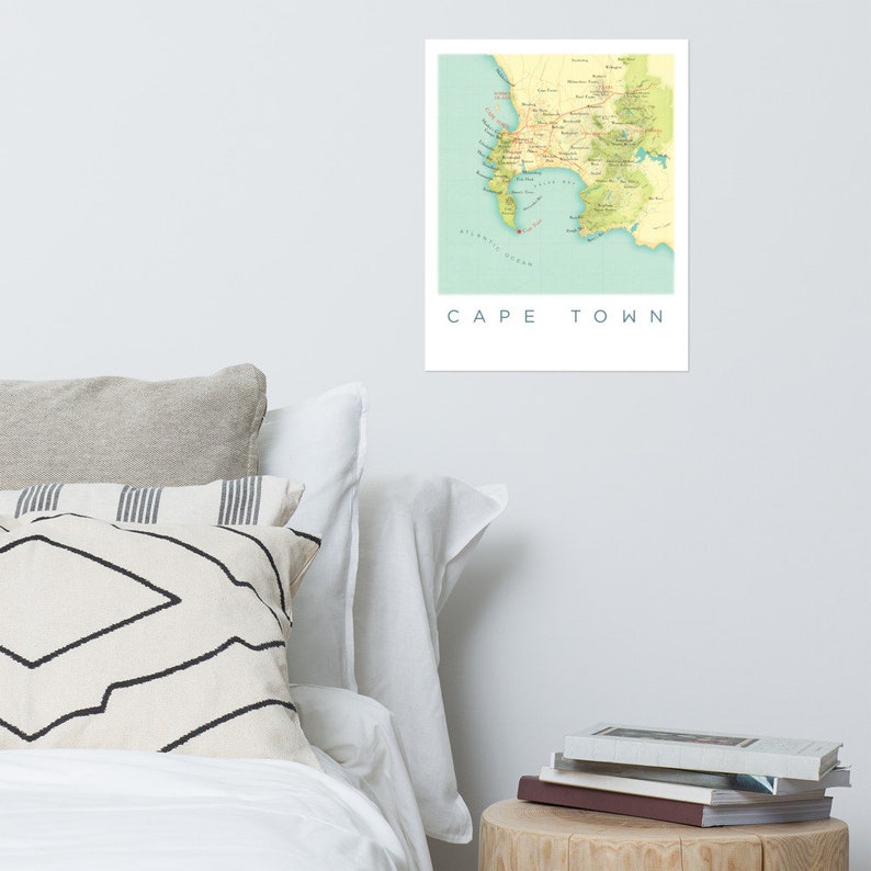 May include: A framed print of a map of Cape Town, South Africa, in shades of yellow, green, and blue. The map shows the coastline, roads, and geographical features. The words "CAPE TOWN" are printed in a clean, sans-serif font below the map.