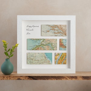 May include: A white framed artwork featuring vintage map pieces arranged in a grid. The maps are in various rectangular shapes, showcasing different locations. The text "Happy Memories Were Made Here" is written in cursive on the white background.
