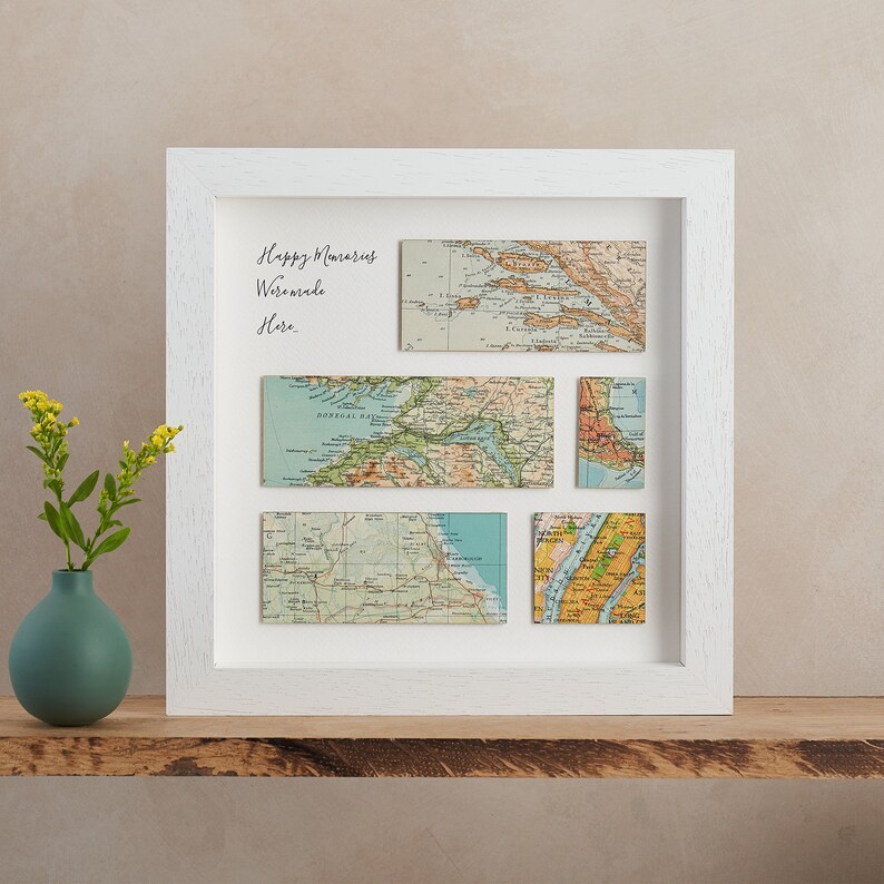May include: A white framed artwork featuring vintage map pieces arranged in a grid. The maps are in various rectangular shapes, showcasing different locations. The text "Happy Memories Were Made Here" is written in cursive on the white background.