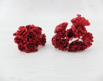 May include: Two clusters of deep red artificial flowers, each composed of multiple small, tightly packed rose-like blooms with layered petals. The dark crimson blossoms are arranged in dense, rounded bunches, showcasing a rich, uniform color throughout.