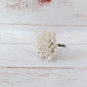 Puede incluir: Un ramo de pequeñas rosas de papel blanco sobre un fondo de madera blanco.