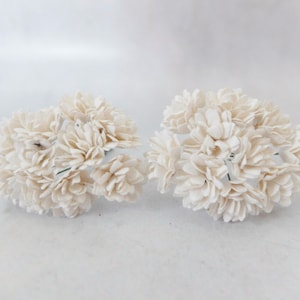 Op de afbeelding: Twee bosjes witte papieren bloemen met een delicaat, gelaagd ontwerp. De bloemen zijn in een cluster gerangschikt en hebben een zachte, natuurlijke uitstraling.