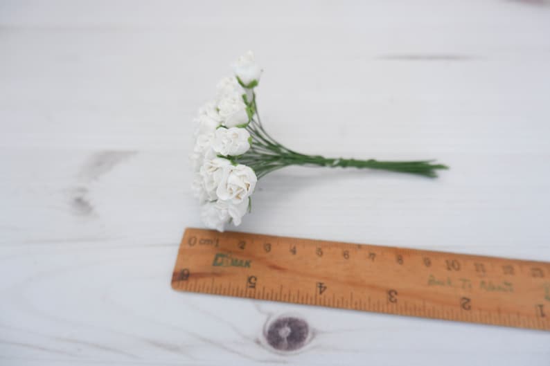 May include: A bunch of small white paper roses with green stems. The roses are arranged in a cluster and are about 2 inches in diameter.