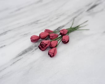 Puede incluir: Un ramo de pequeñas flores de papel rosa con tallos verdes sobre un fondo de mármol blanco.