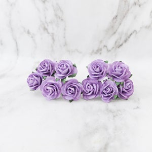 May include: A cluster of eight small, lavender paper roses with green paper leaves. The roses are arranged in two rows on a white marble surface.