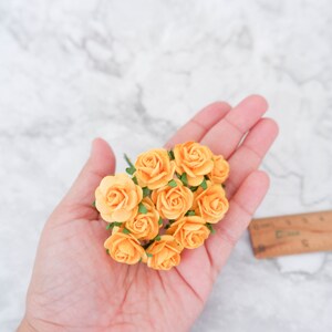 May include: A bunch of small, peach-colored paper roses with green leaves. The roses are held in a hand.