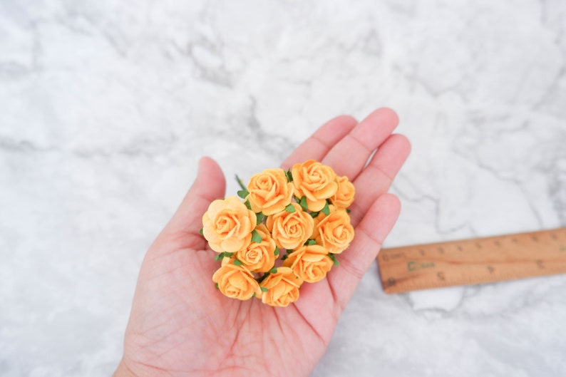 May include: A bunch of small, peach-colored paper roses with green leaves. The roses are held in a hand.