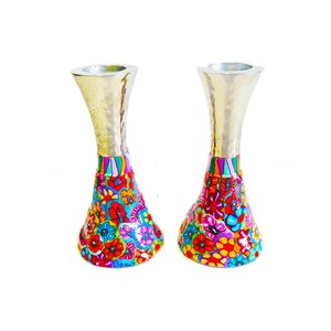 May include: A pair of candlestick holders featuring a metallic, hammered gold-tone upper section and a wide, flared base decorated with a vibrant, multi-colored floral pattern in shades of red, blue, yellow, and pink against a white background.