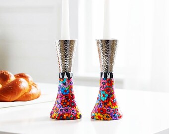 May include: Two candle holders with white candles. The holders have a silver hammered top, a black and white striped band, and a base decorated with colorful floral patterns. The holders are on a white surface.