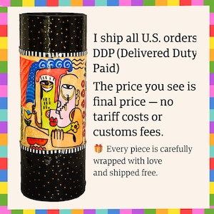 May include: A cylindrical vase featuring a central band decorated with a colorful abstract face illustration in shades of yellow, blue, red, and orange. The top and bottom sections of the vase are black with small yellow dots and white stripes.