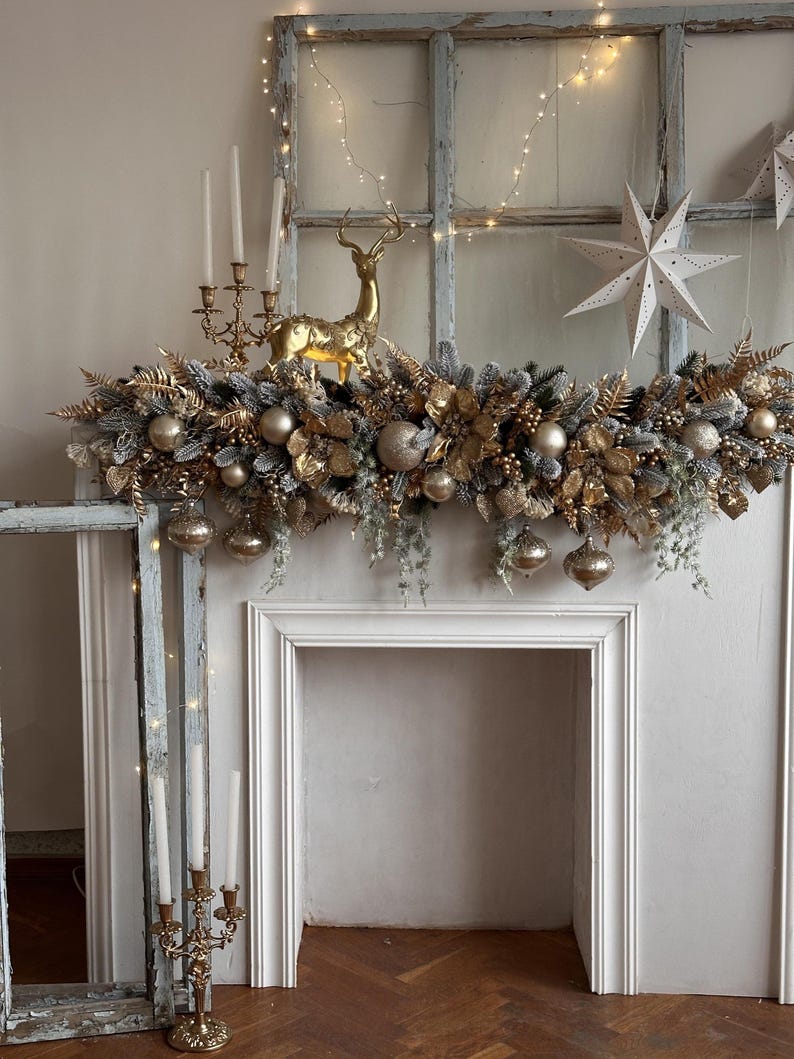 May include: A festive Christmas mantelpiece decorated with gold and silver ornaments, faux greenery, and a golden reindeer figurine. The mantel also features a candelabra with white candles and a string of fairy lights, creating a warm, inviting holiday display.
