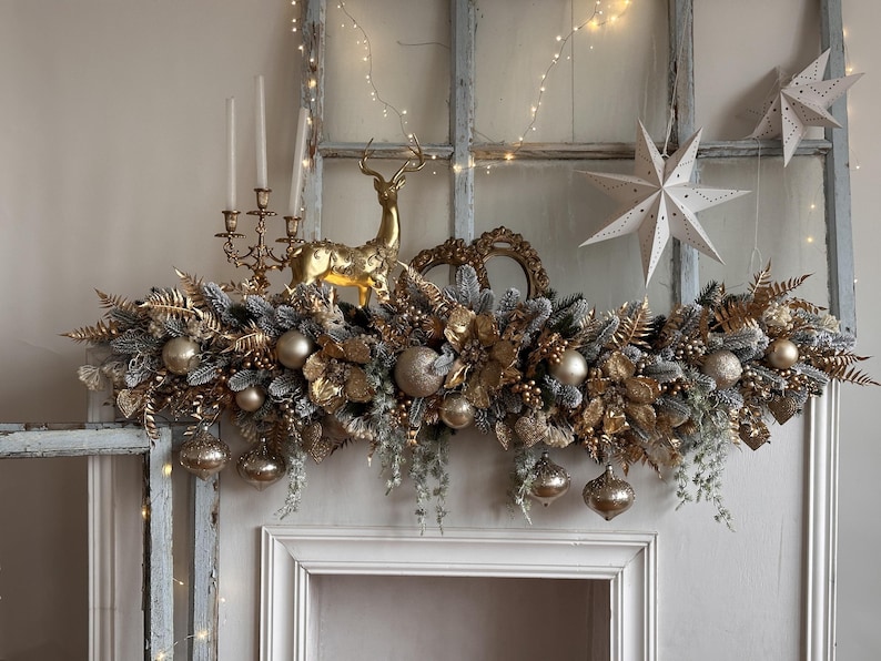 May include: A festive Christmas mantel arrangement featuring a garland of gold and silver foliage, gold ornaments, and a golden reindeer figurine. The display includes white paper star decorations and a candelabra.