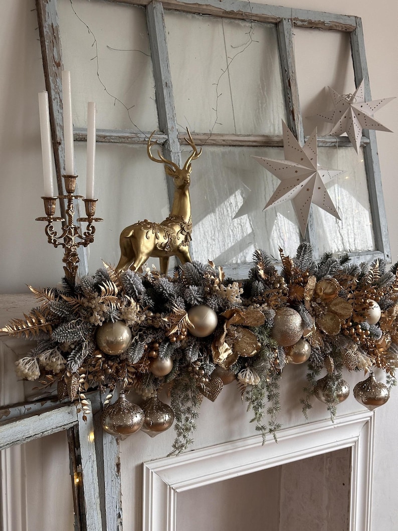 May include: A festive Christmas mantel arrangement featuring a gold reindeer figurine, a gold candelabra with white candles, and hanging ornaments. The arrangement includes gold and silver decorative elements, including star-shaped decorations and a garland.