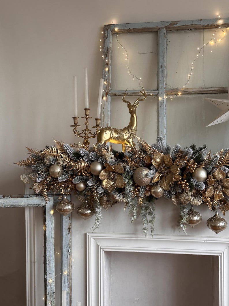 May include: A festive Christmas mantelpiece decoration featuring a gold reindeer figurine, gold ornaments, and faux greenery. The arrangement includes gold-colored baubles, leaves, and berries, creating a luxurious holiday display. The mantel is decorated with string lights.