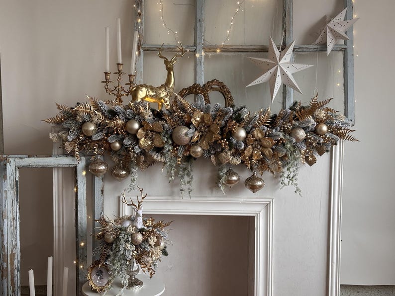May include: A festive Christmas mantelpiece arrangement featuring gold and silver ornaments, faux foliage, and a golden reindeer figurine. The display includes hanging ornaments, decorative stars, and a candelabra.