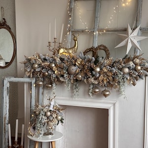 May include: A festive Christmas mantelpiece decorated with gold and silver ornaments, including baubles, a golden reindeer, and a star. The arrangement includes faux greenery and hanging ornaments, creating a luxurious holiday display.