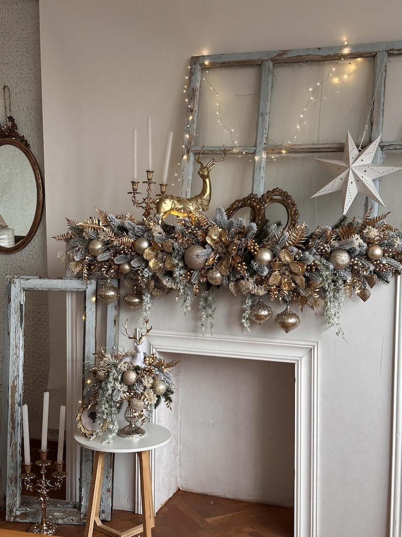 May include: A festive Christmas mantelpiece decorated with gold and silver ornaments, including baubles, a golden reindeer, and a star. The arrangement includes faux greenery and hanging ornaments, creating a luxurious holiday display.