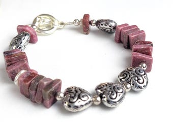 May include: A pink and silver bracelet with heart-shaped charms and rectangular beads. The bracelet is made of metal and stone.