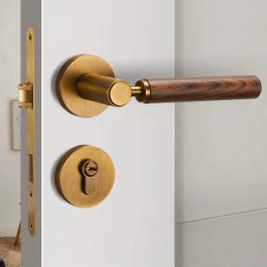 Peut inclure: Ensemble de poignées de porte avec une finition en laiton et une poignée en bois. L'ensemble comprend une poignée ronde, un cache-trou de serrure et une plaque de pêne dormant. La poignée en bois a un grain brun foncé.